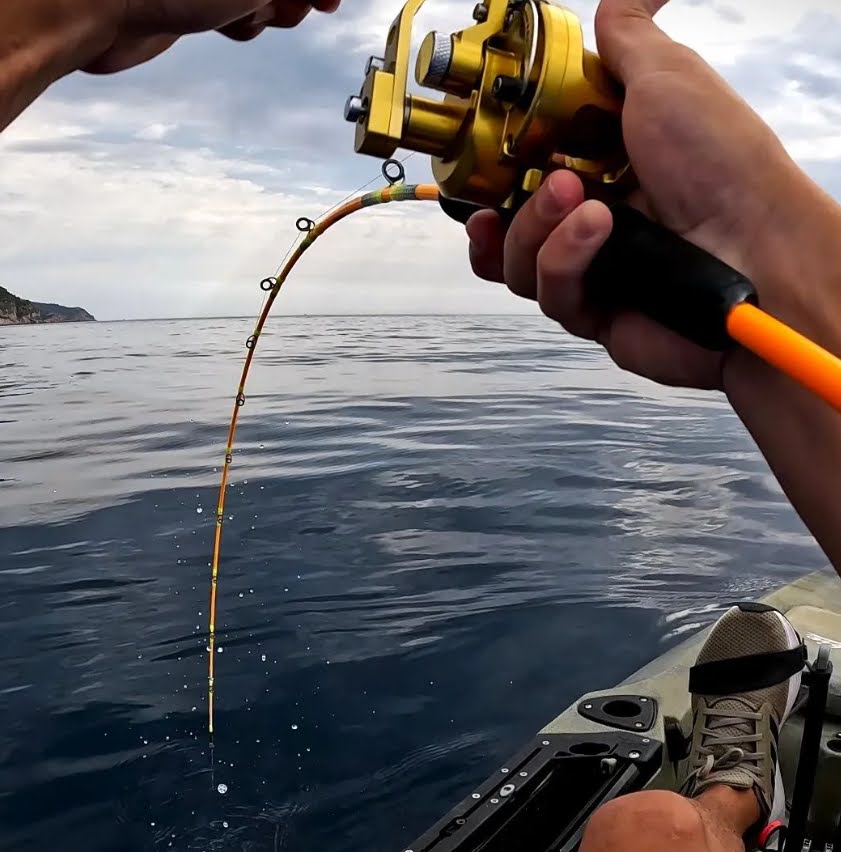 Pesca a jigging desde kayak donde se aprecia una bonita curvatura de la caña en acción de pesca